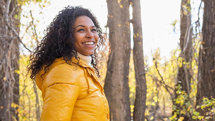 Smiling woman wearing a yellow jacket in the woods.